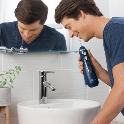 A Man using cordless water flosser over a sink