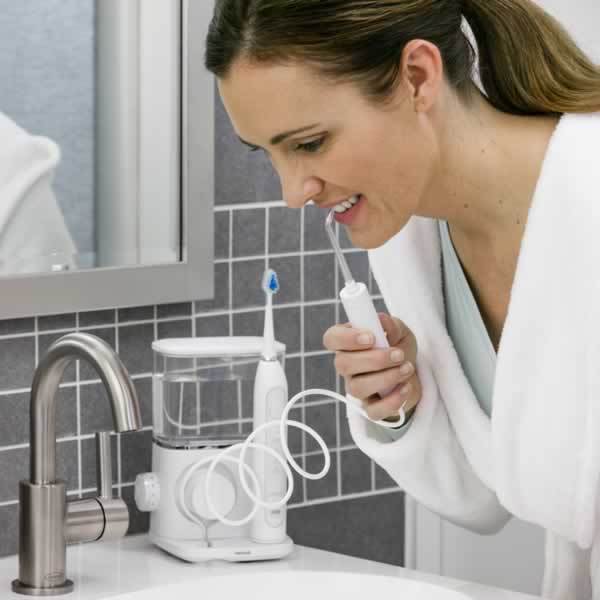 A woman using countertop water flosser over a sink