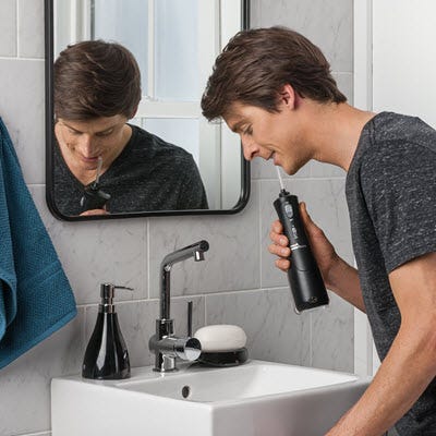 A man using cordless water flosser over a sink