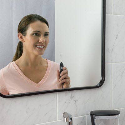 A woman smiling in the mirror holding water flosser