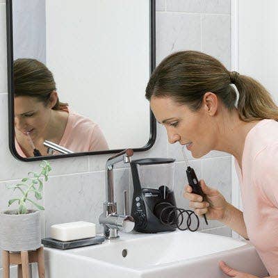 A woman using countertop water flosser over a sink