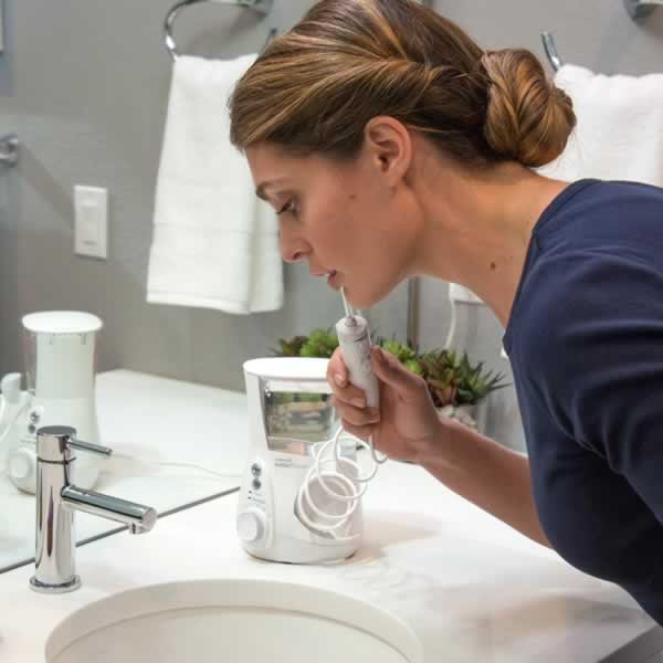 A woman using countertop water flosser over a sink